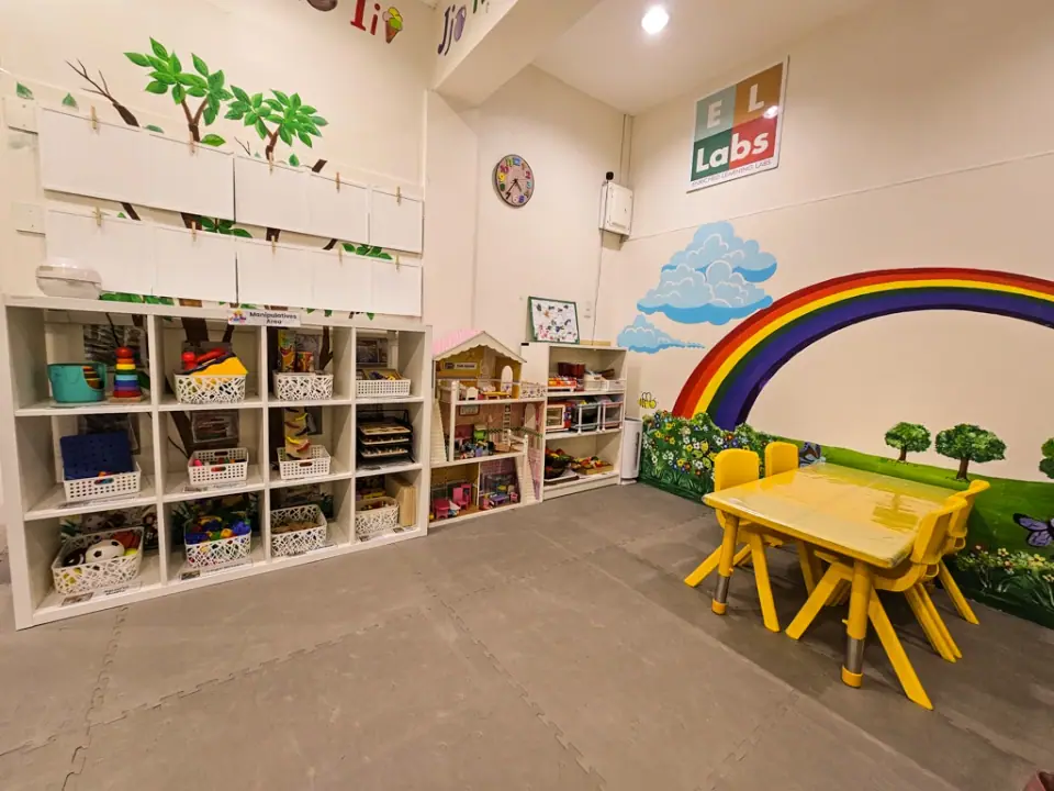 Main classroom with low shelves, small tables and a rainbow mural