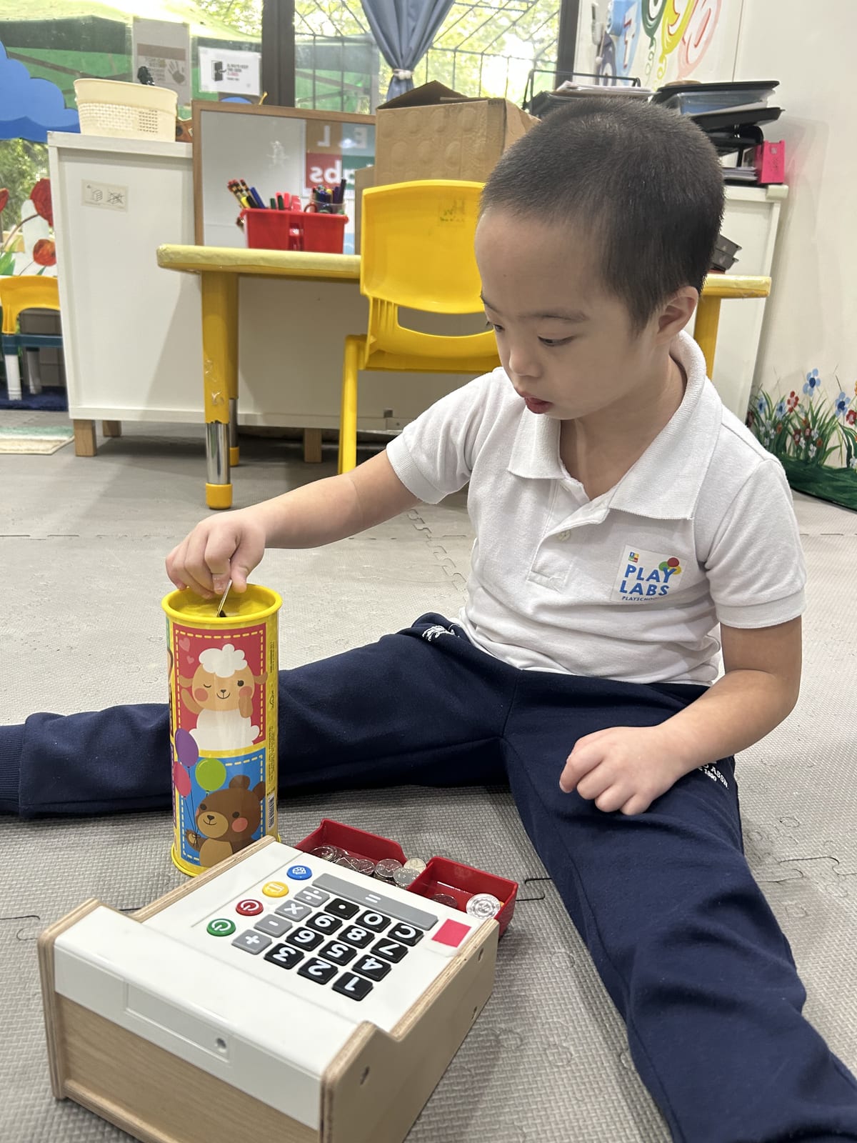 Child dropping play coins into a bank next to a toy cash register during a C.O.R.E. session